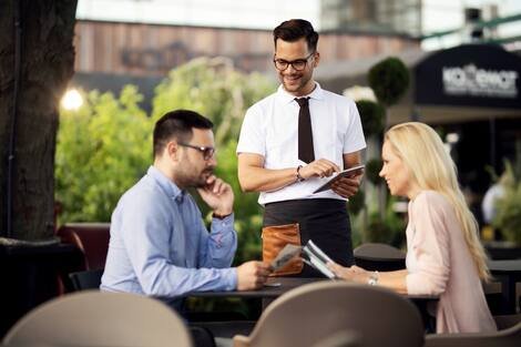 Young happy waiter serving a couple in an outdoor cafe. Young happy waiter serving a couple in an outdoor cafe.
