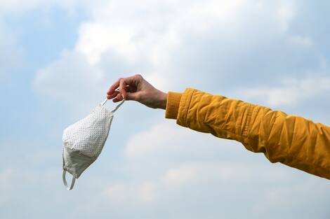 Woman is holding the textile home made face mask used for protection against viruses while walking in the nature. Symbol for protest against regulations or freedom after end of pandemic. Woman is holding the textile home made face mask used for protection against viruses while walking in the nature. Symbol for protest against regulations or freedom after end of pandemic.